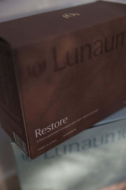 deep recovery sleep supplement. A close-up of a brown product box for Lunaume Restore, with the brand name partially visible and the product name printed in white text.
