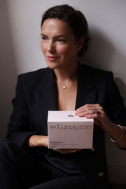 hormonal balance supplement for women. A woman in a black blazer holds a white box of Lunaume Balance against a neutral gray background.
