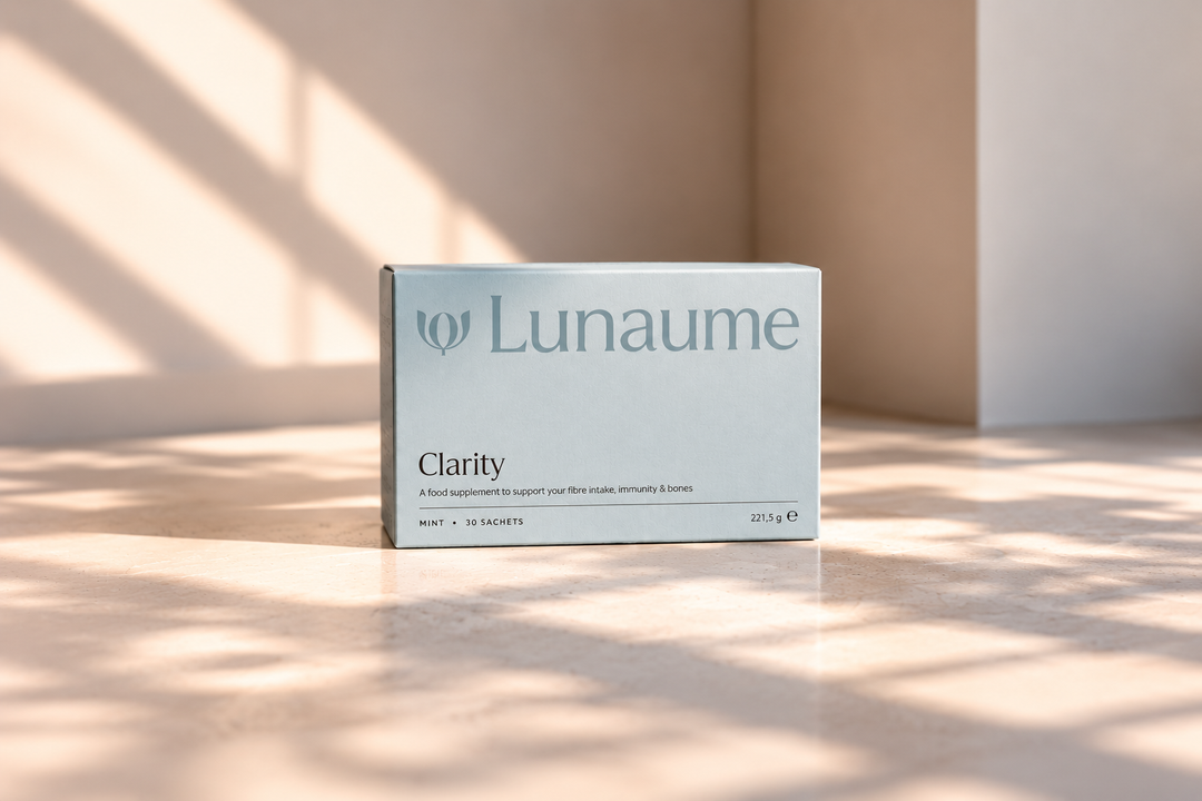 A light blue-gray box of Lunaume Clarity dietary supplement standing on a warm beige surface with soft window shadows cast across the scene.