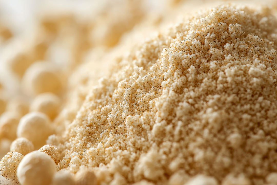 A close-up shot of a mound of light tan powder, with small pale round beads visible along the left side and blurred in the background.